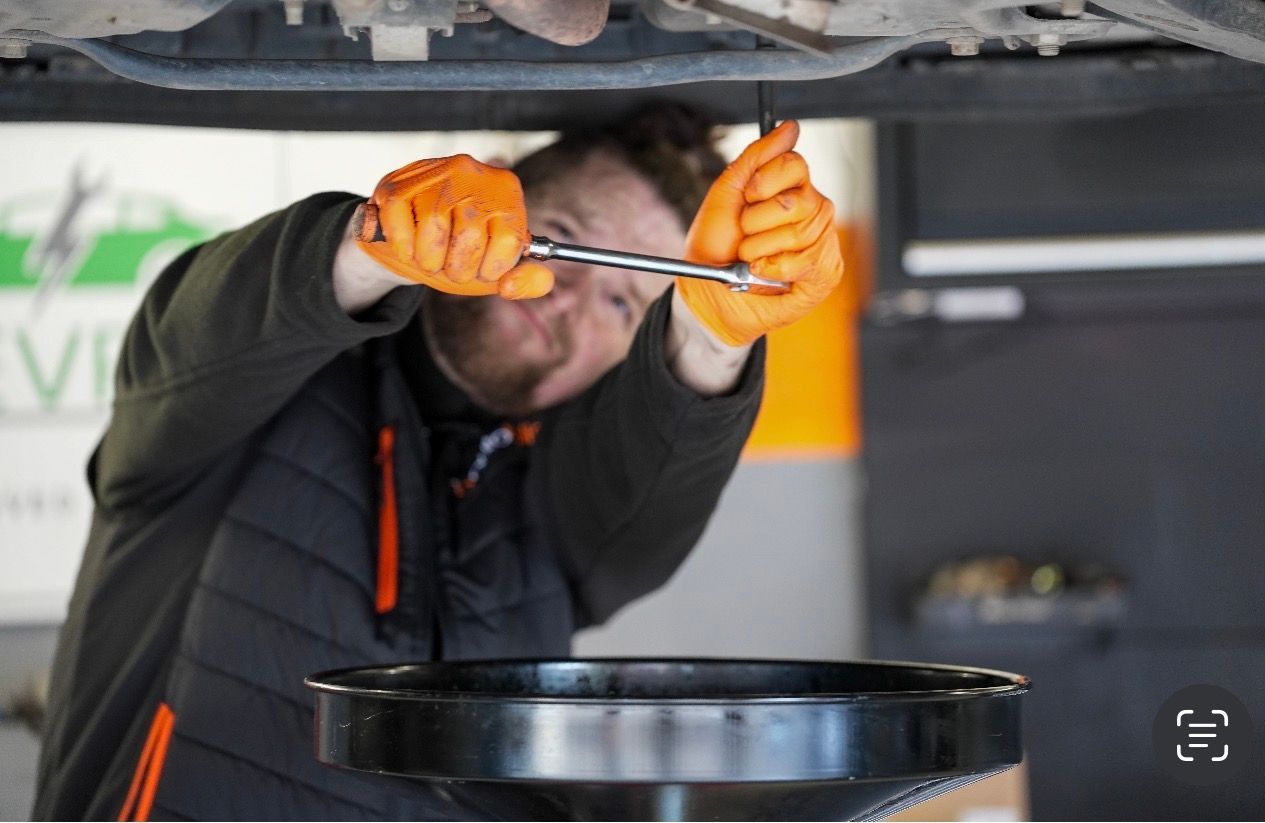 A mechanic in a blue uniform uses a handheld diagnostic tool to inspect a car engine in a professional garage.