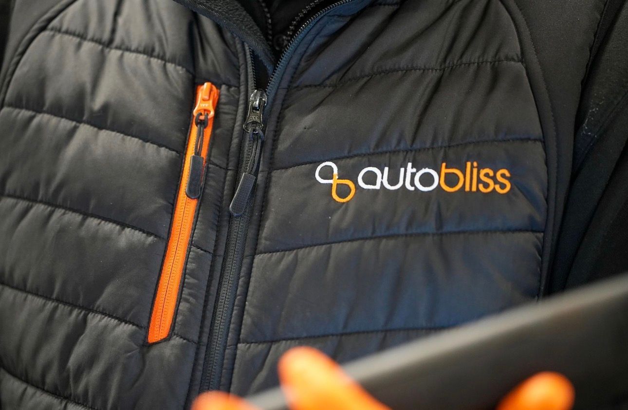 A close-up shot of a person wearing a black quilted vest with an orange zipper and an embroidered 
