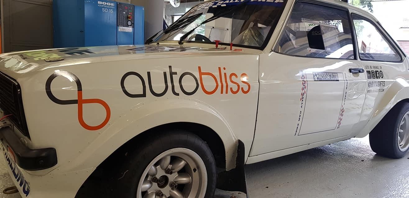 A white, modified Ford Escort rally car parked indoors, featuring an 