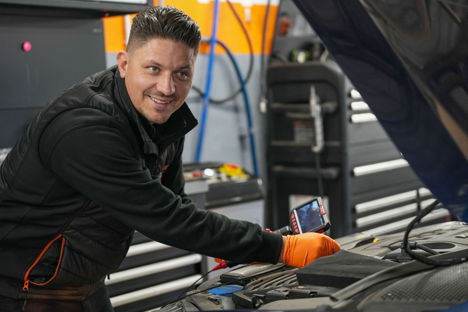 Two mechanics in blue uniforms smile and shake hands inside an auto repair shop.