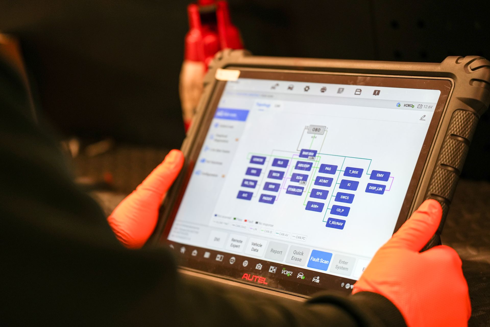 A person wearing orange gloves holds a rugged tablet displaying a diagnostic network flowchart in a professional setting.