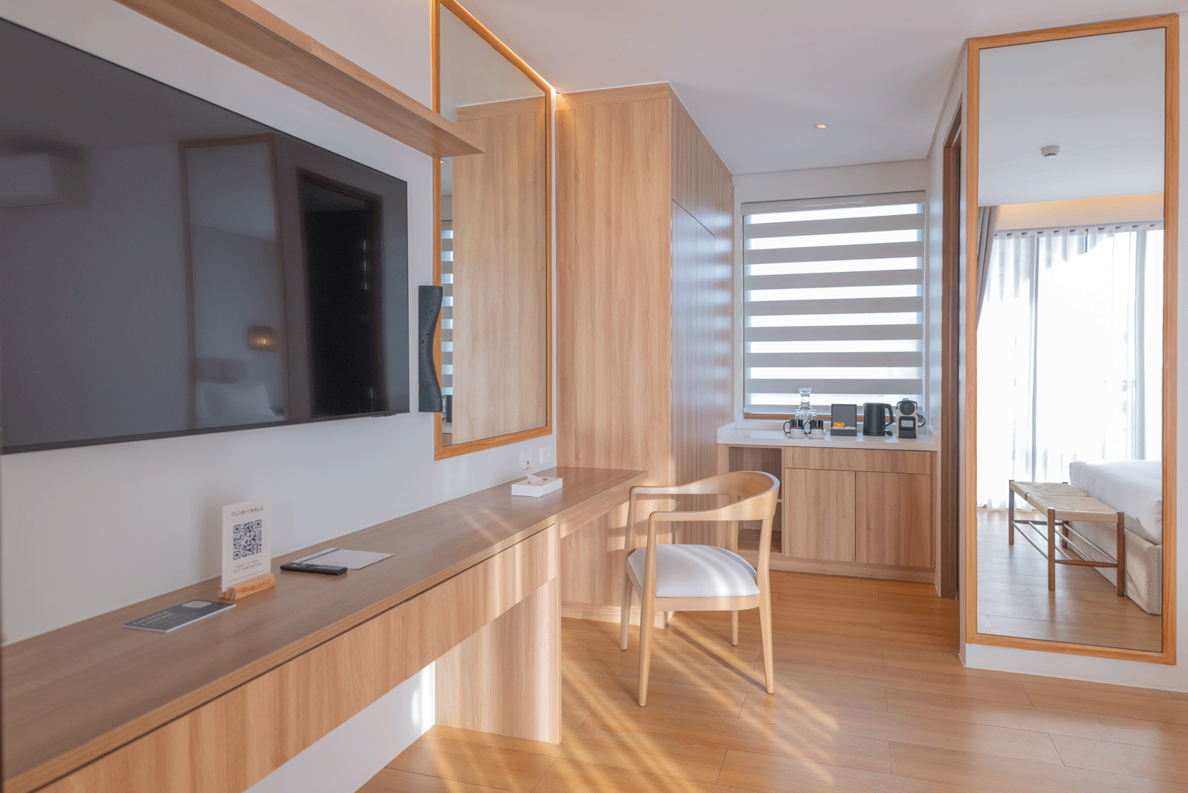 Modern hotel room with wooden desk, flat-screen TV, and natural light