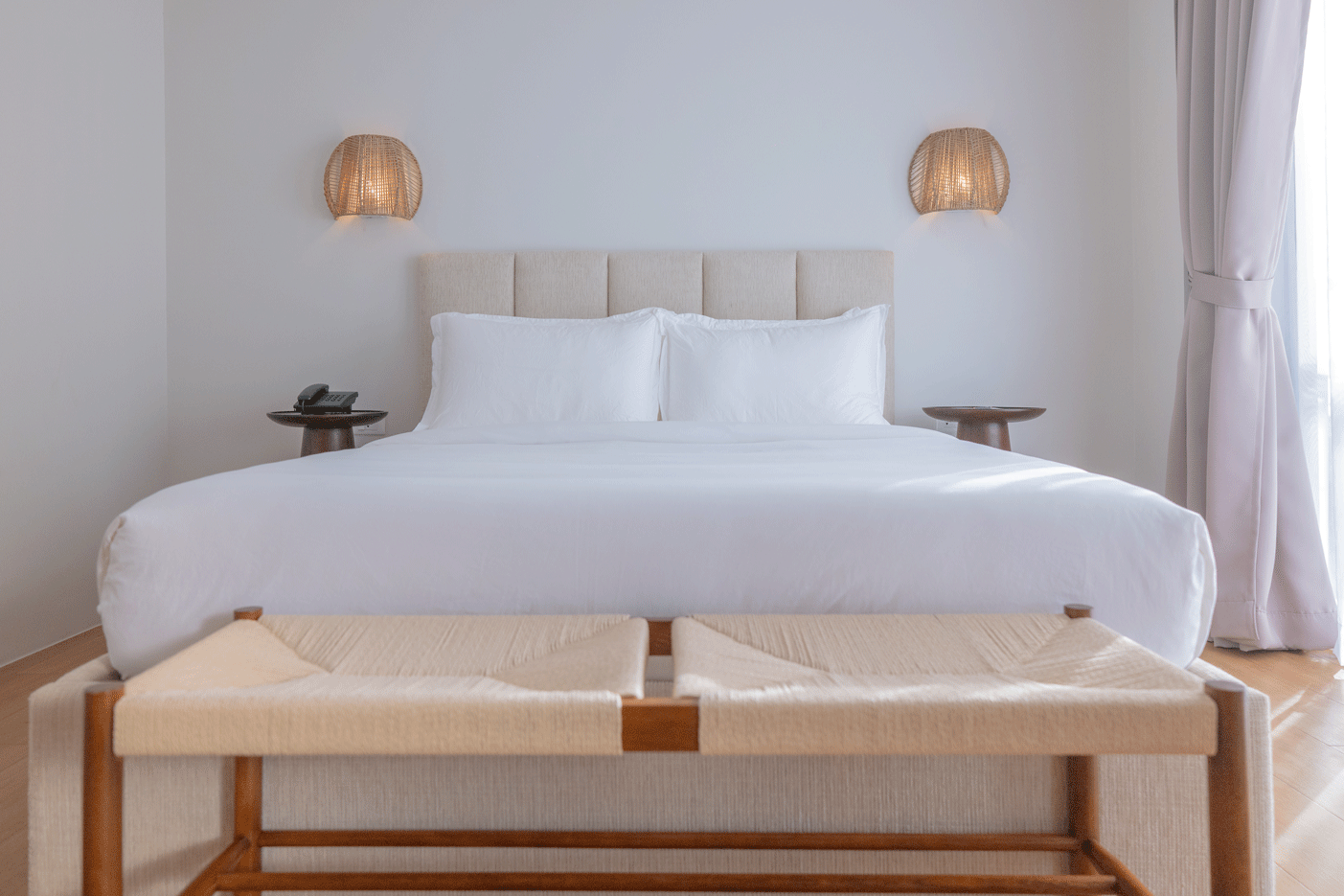 Minimalist king bedroom with white linens and rattan wall sconces at Harves