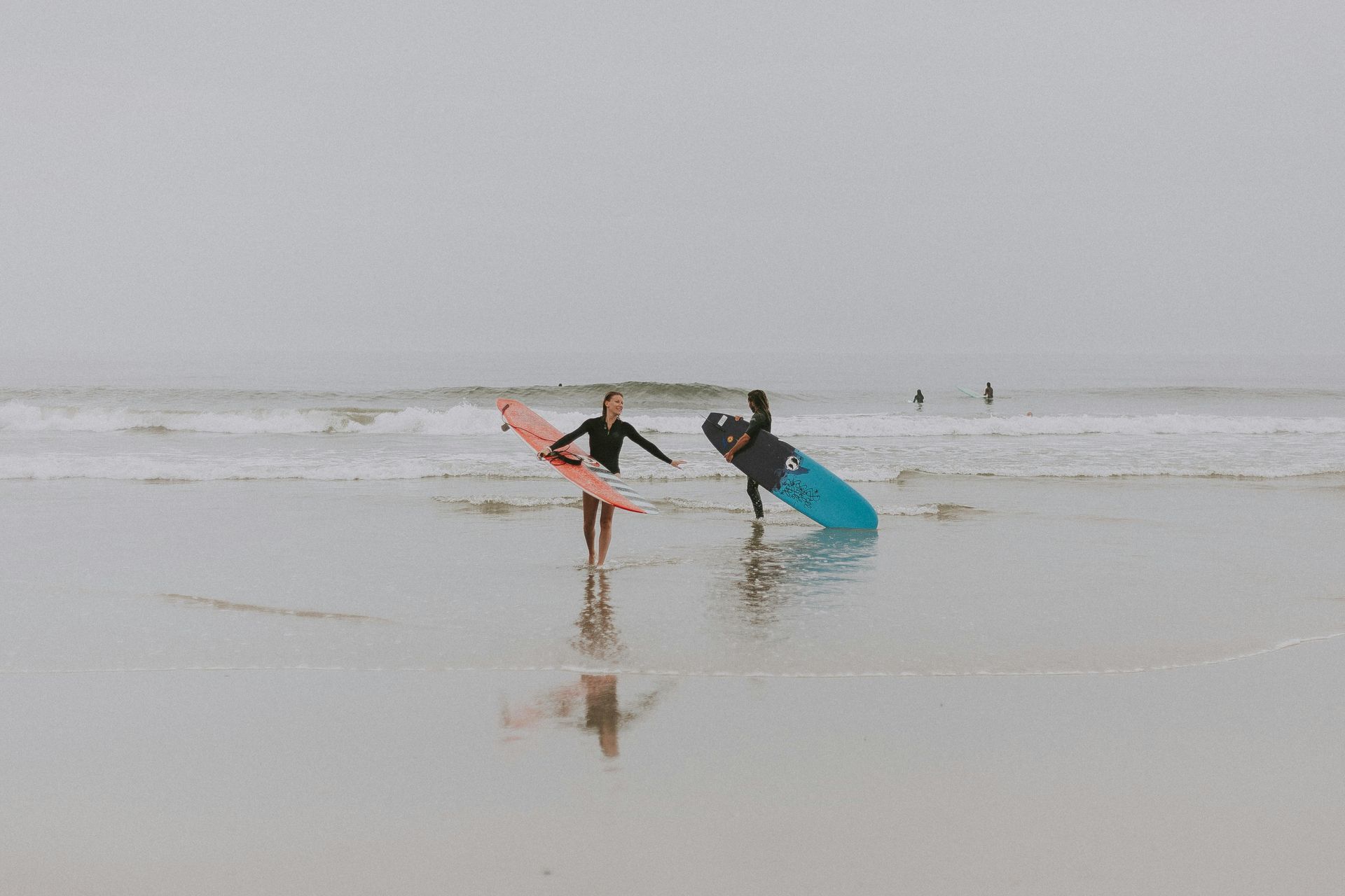 Two people with surfboards wading in shallow water on a foggy beach
