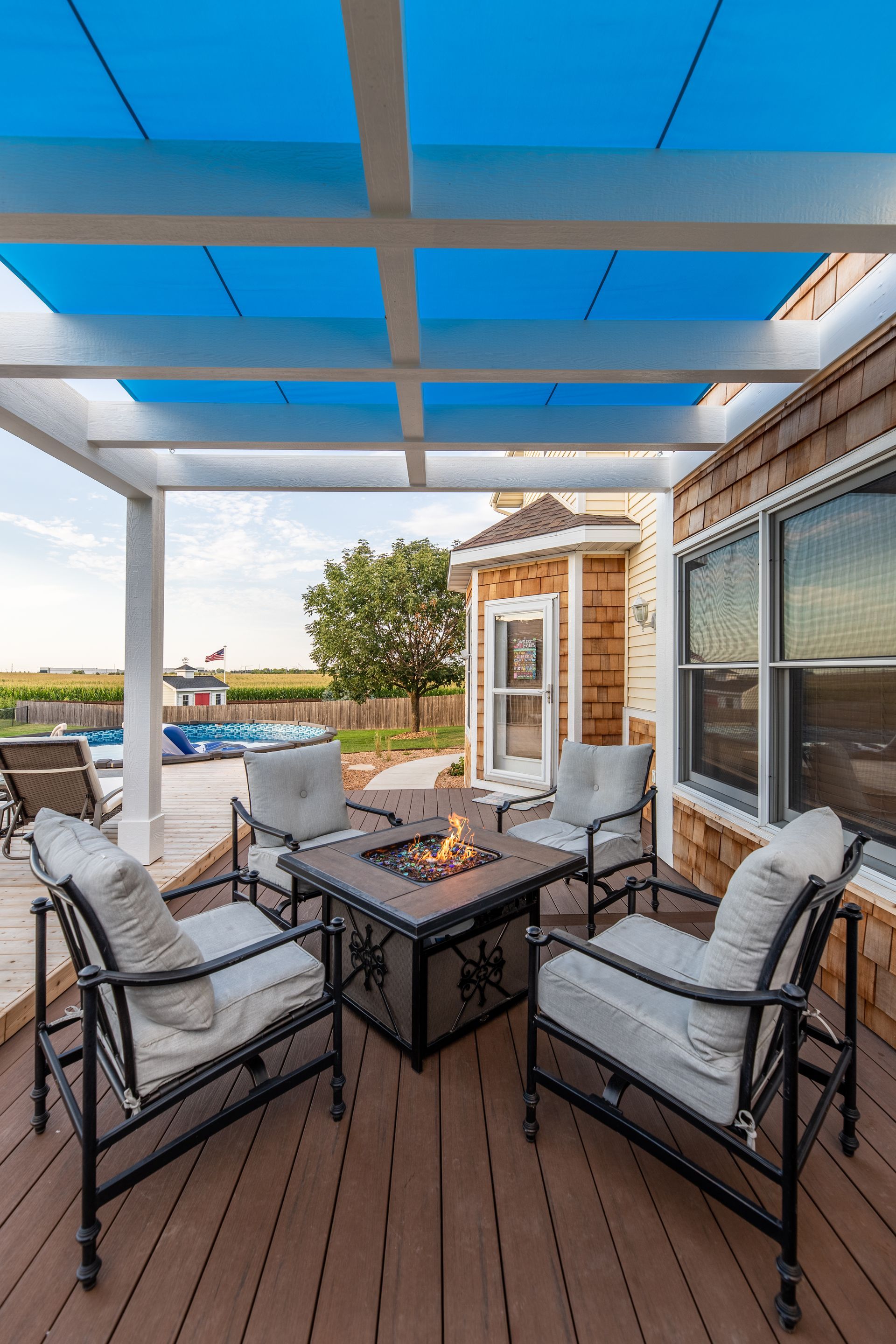 There is a fire pit on the deck under a pergola.