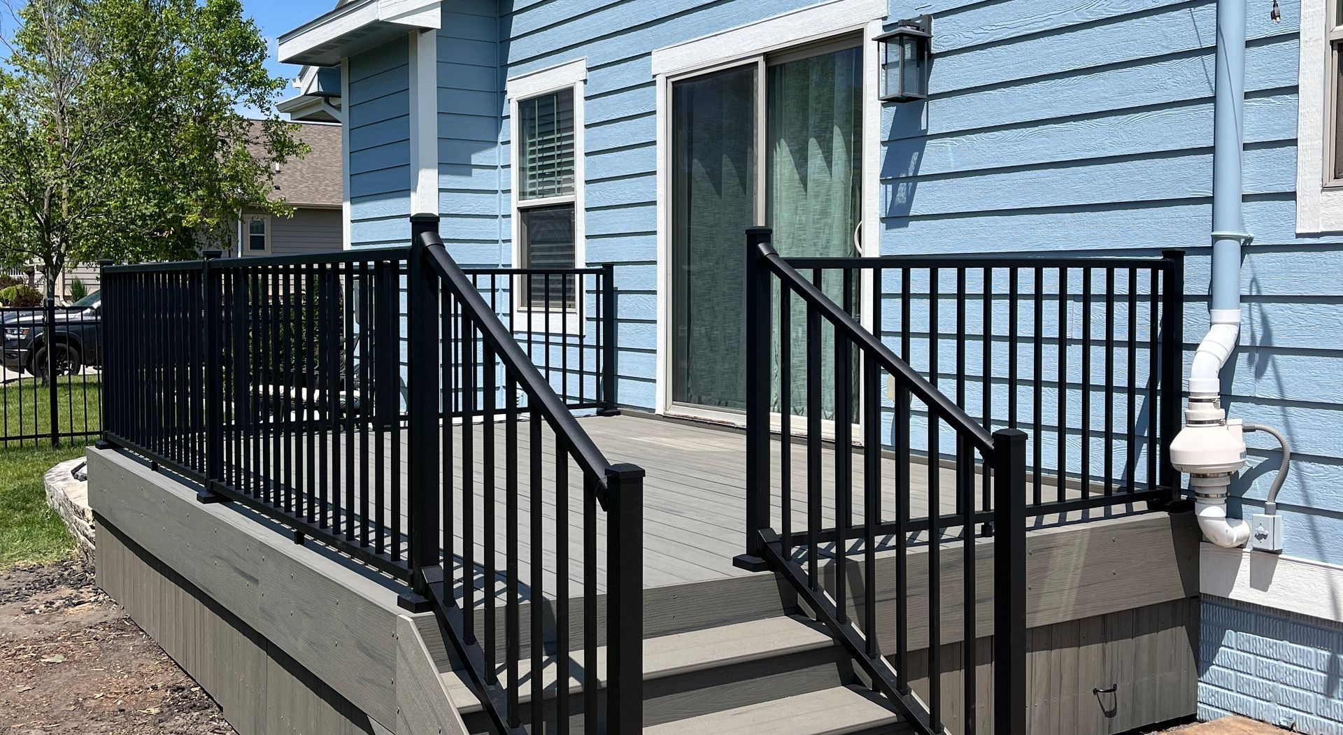 A blue house with a black railing and stairs leading up to a grey composite deck.