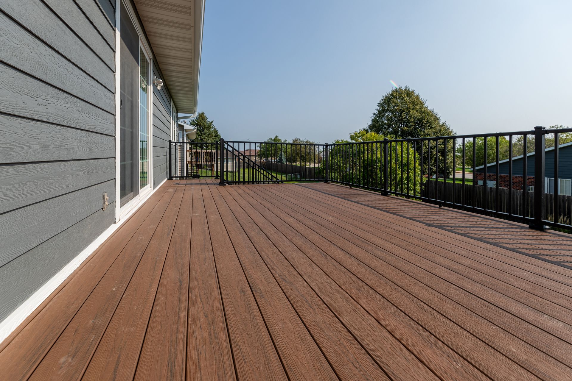 A large wooden deck with a metal railing on the side of a house.