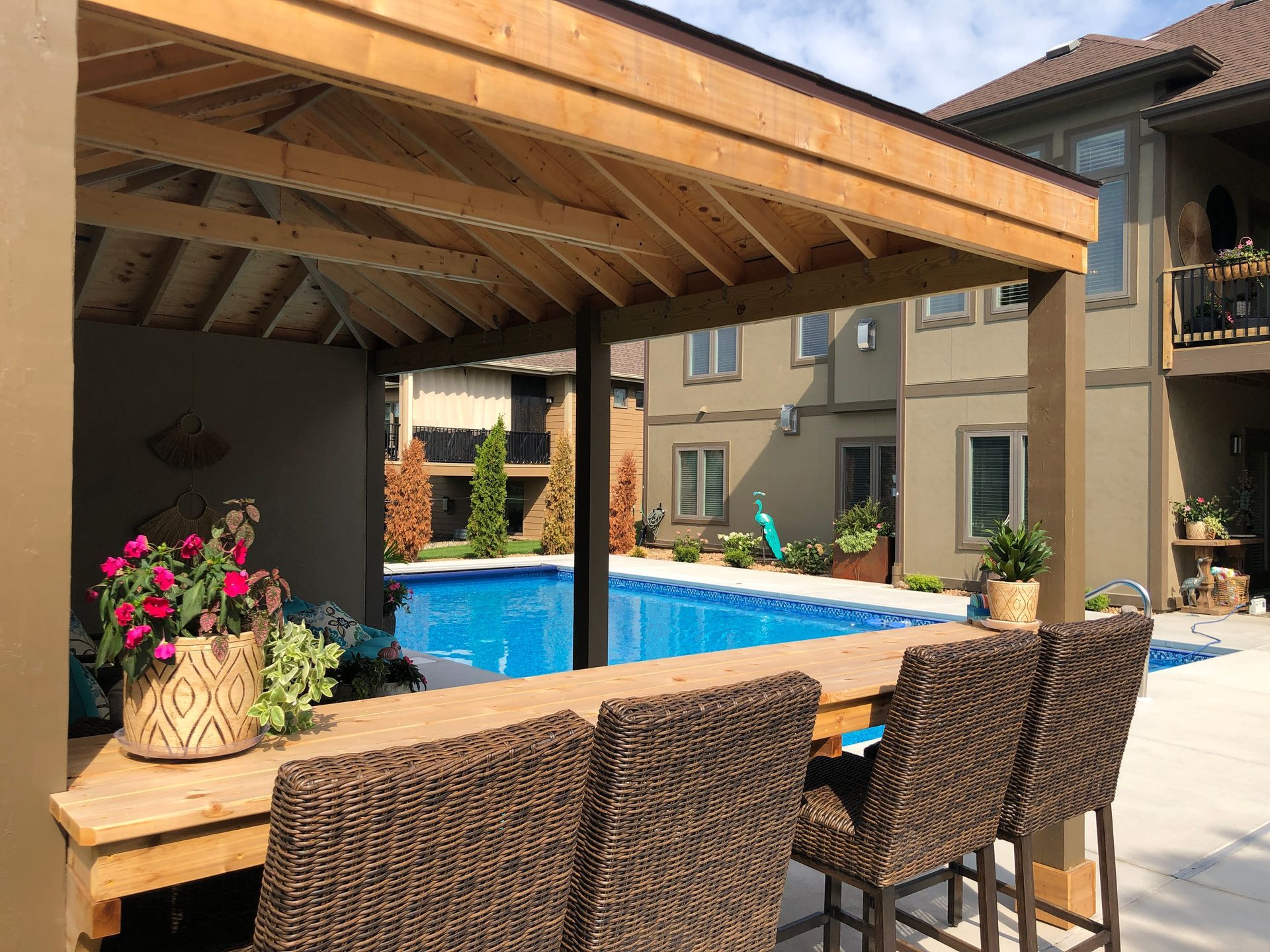A wooden gazebo overlooking a swimming pool with wicker chairs and a table.