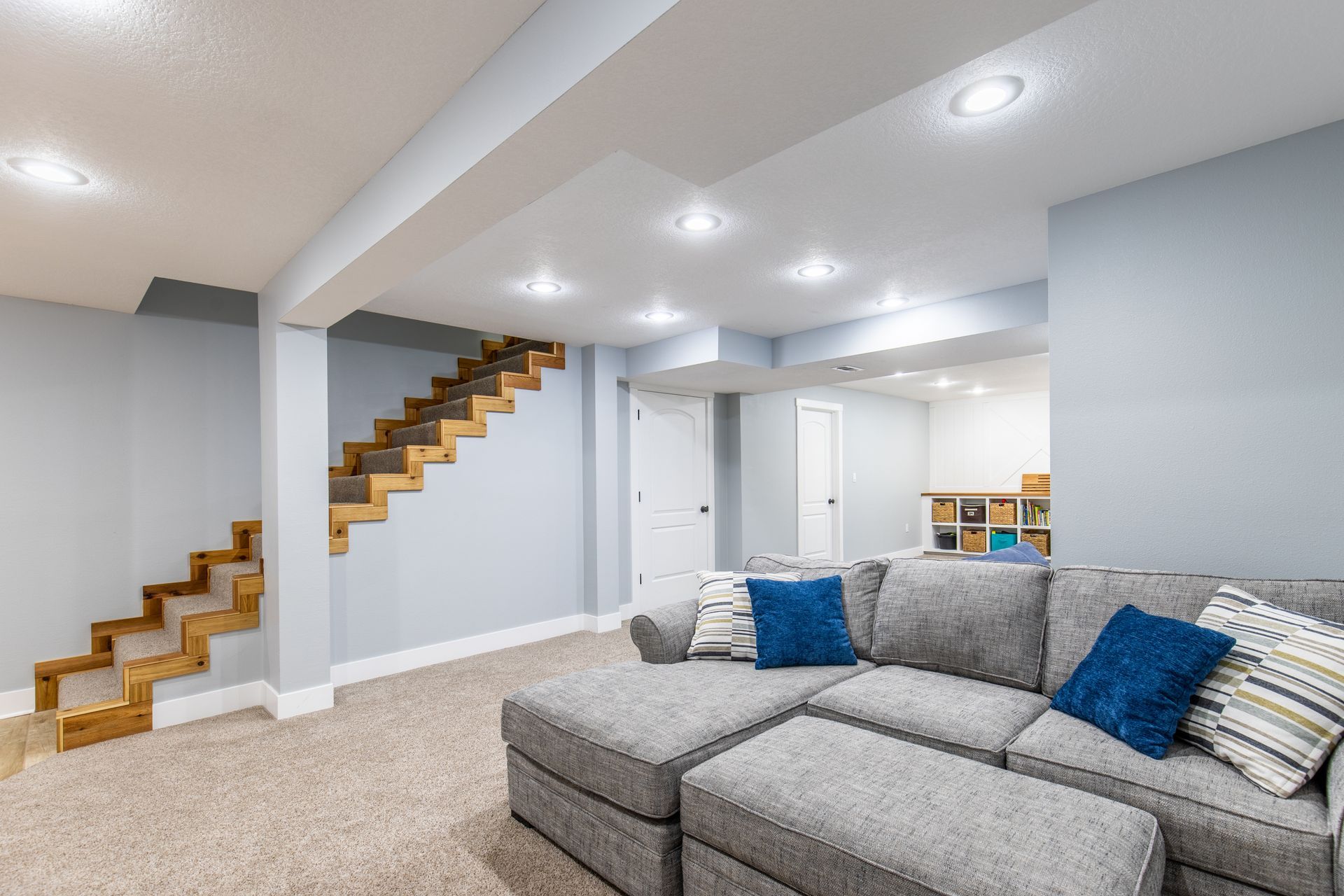 A remodeled living room in a basement with a couch and stairs.