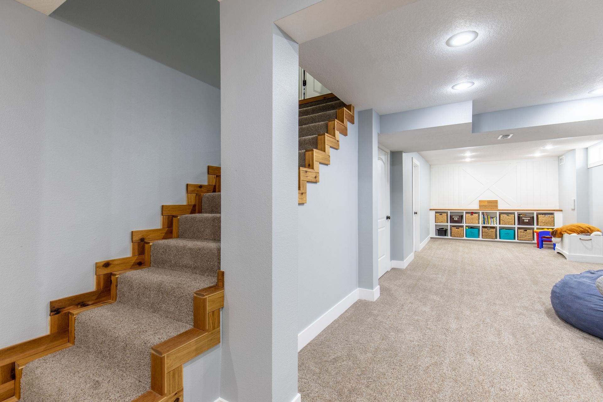 A basement with stairs leading up to the second floor and a carpeted floor.