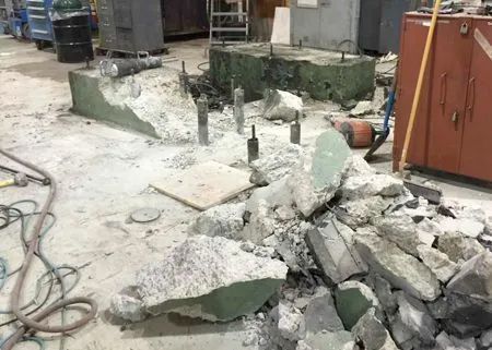 Concrete demolition in a workshop. Debris scattered around metal anchors and a partially dismantled concrete base.