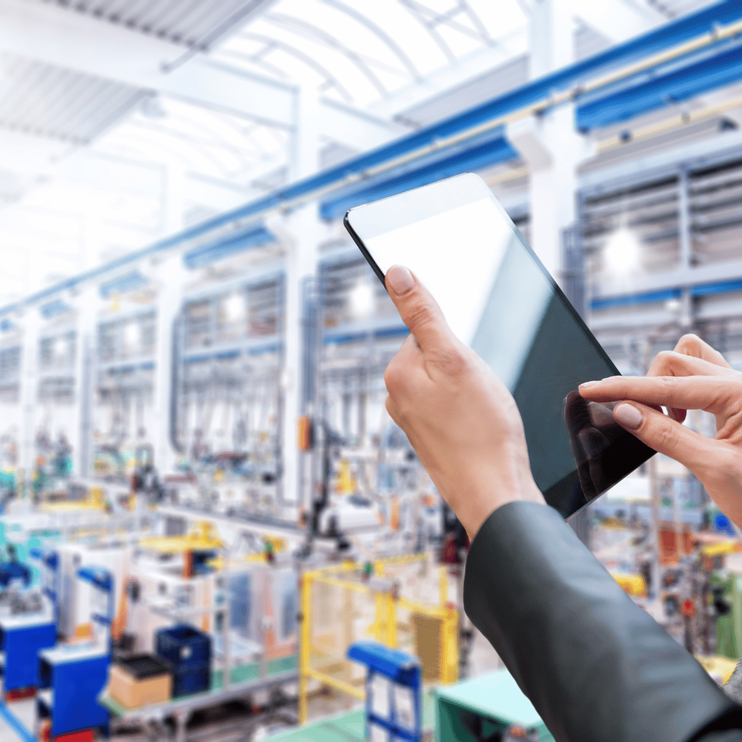 Hands holding a tablet in a bright industrial factory workshop