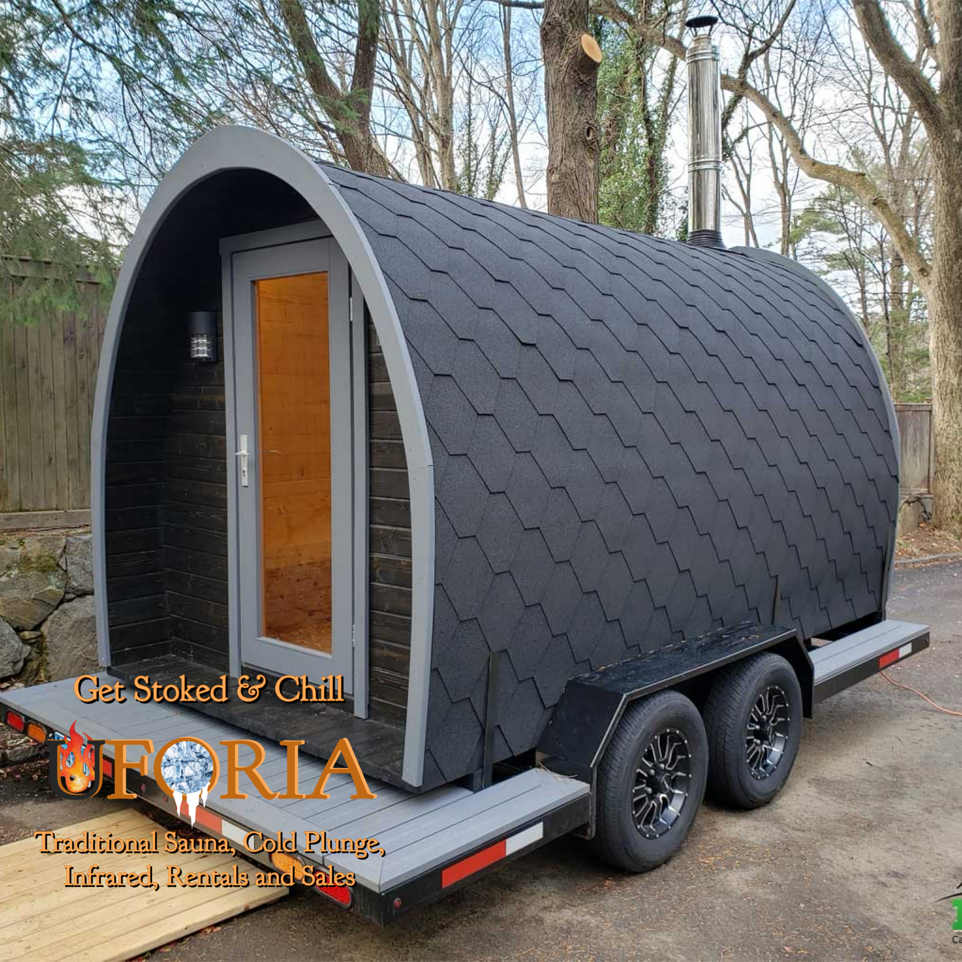 Black arched tiny cabin on a dual-axle trailer in a wooded setting