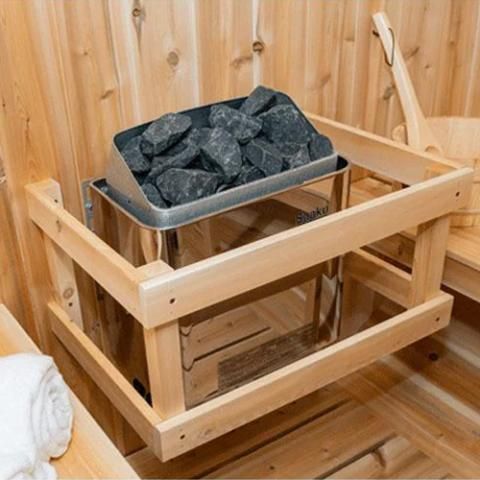 Wood-paneled sauna with a heater filled with black sauna stones inside a wooden safety frame