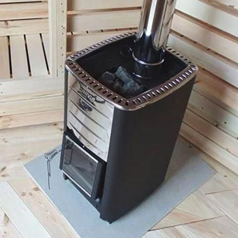 Black sauna stove with metal flue in a wooden sauna room, on a gray floor mat.