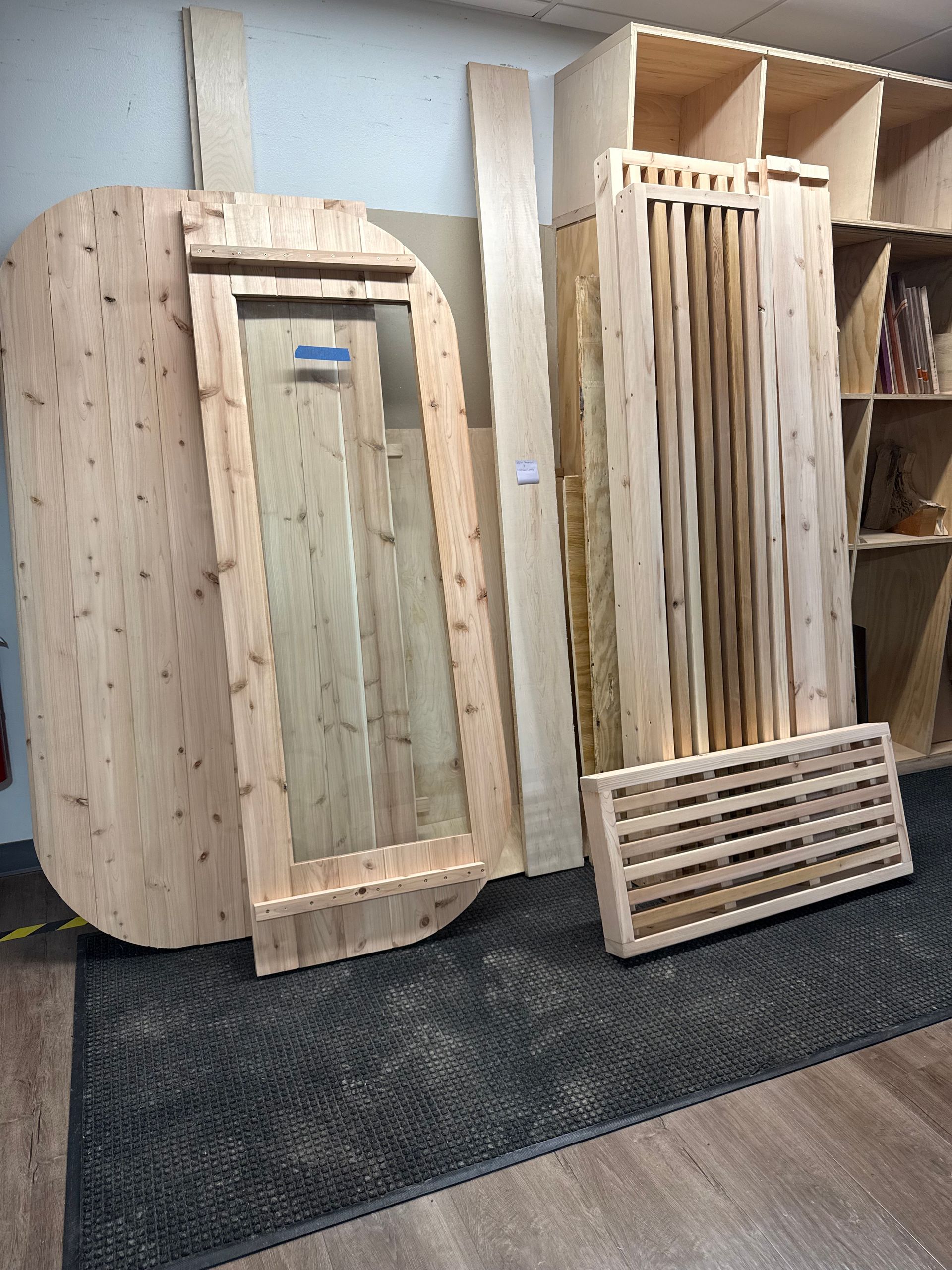 Wooden display booth mockup with vertical slats and a small barred gate panel on a carpeted floor.