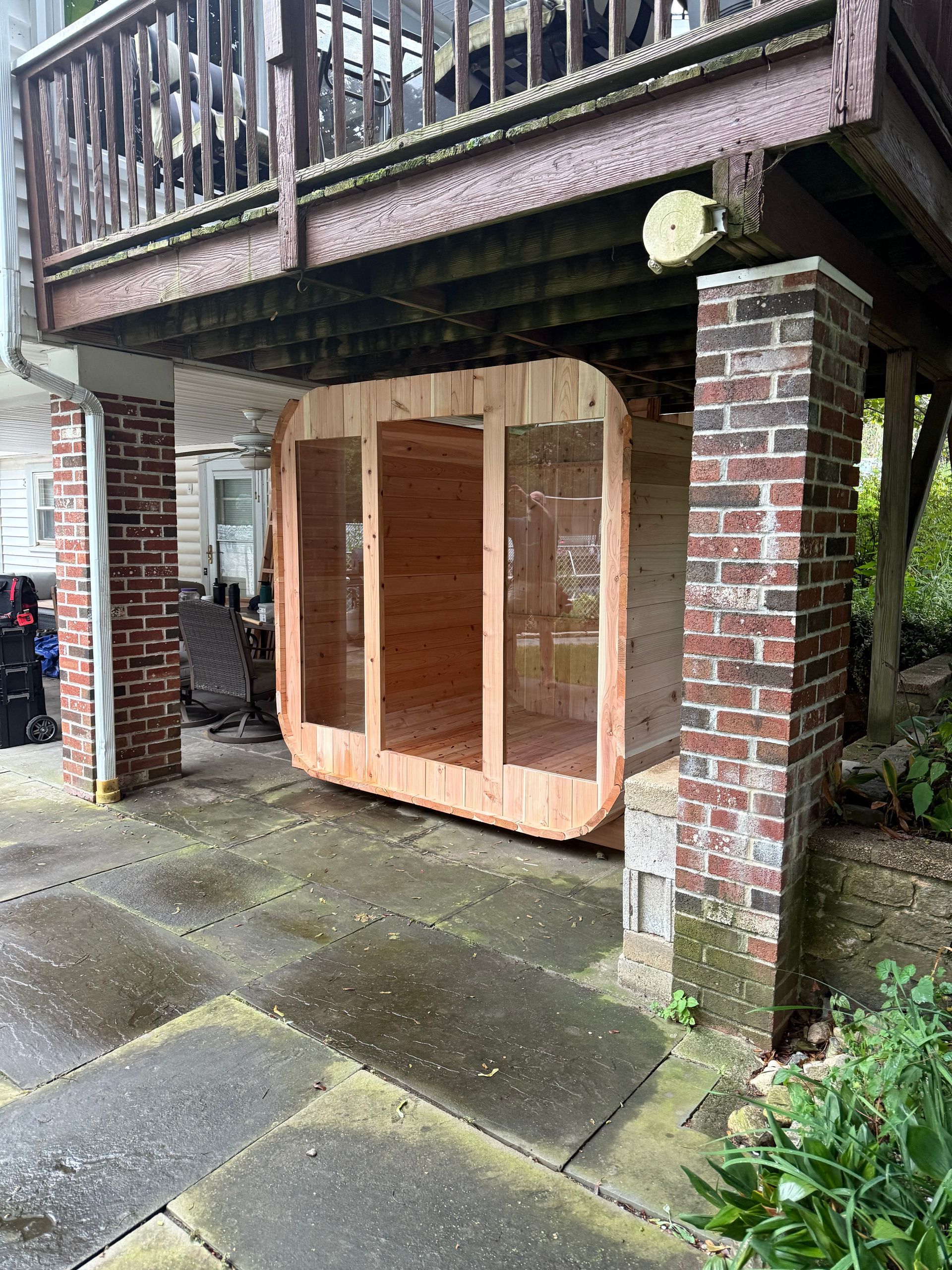 Wooden storage cabinet under a brick balcony in a wet paved courtyard