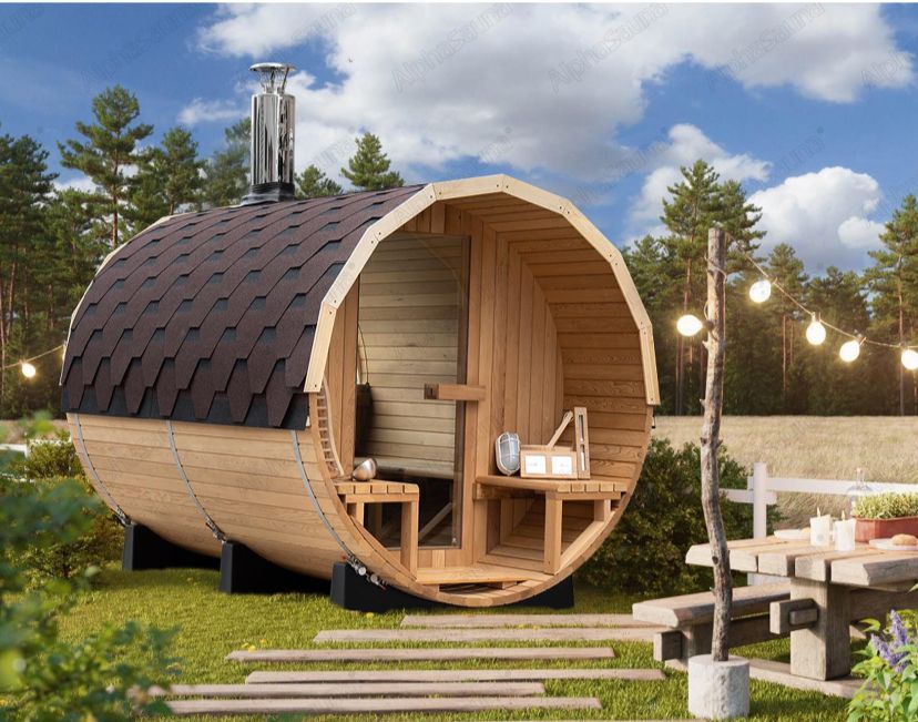 Wooden barrel-shaped sauna cabin outdoors with chimney, benches, and string lights under a cloudy sky