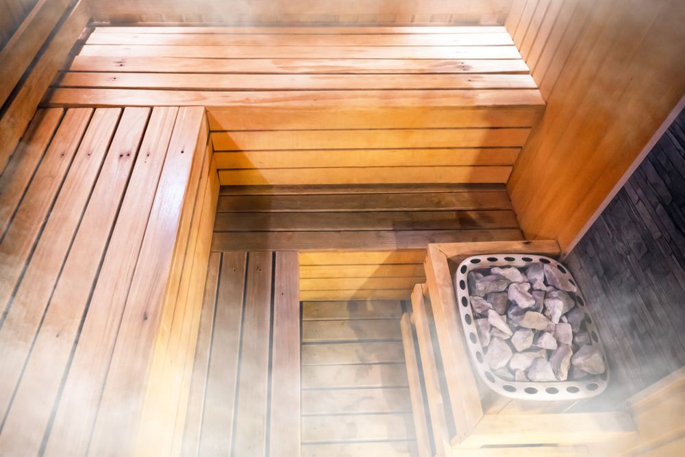 Small wooden sauna cabin with glass doors on a gravel pad in a wooded backyard