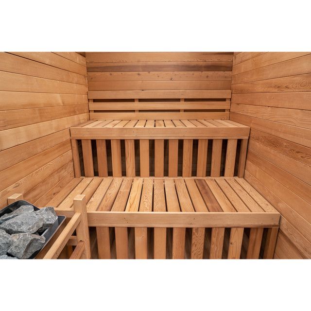 Wood-paneled sauna with tiered wooden benches and a pile of rocks in the corner
