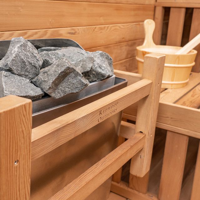 Wooden sauna with a tray of heated stones and a pale wood bucket with ladle