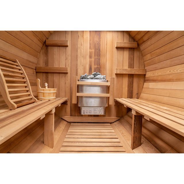 Wood-paneled sauna interior with wooden benches, slatted floor, and heater stones at the back