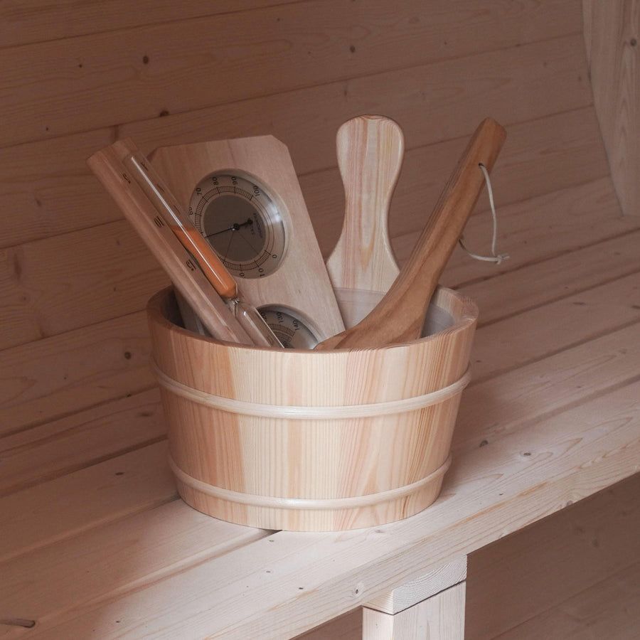 Wooden sauna bucket holding birch whisks, ladle, and a thermometer on a bench.