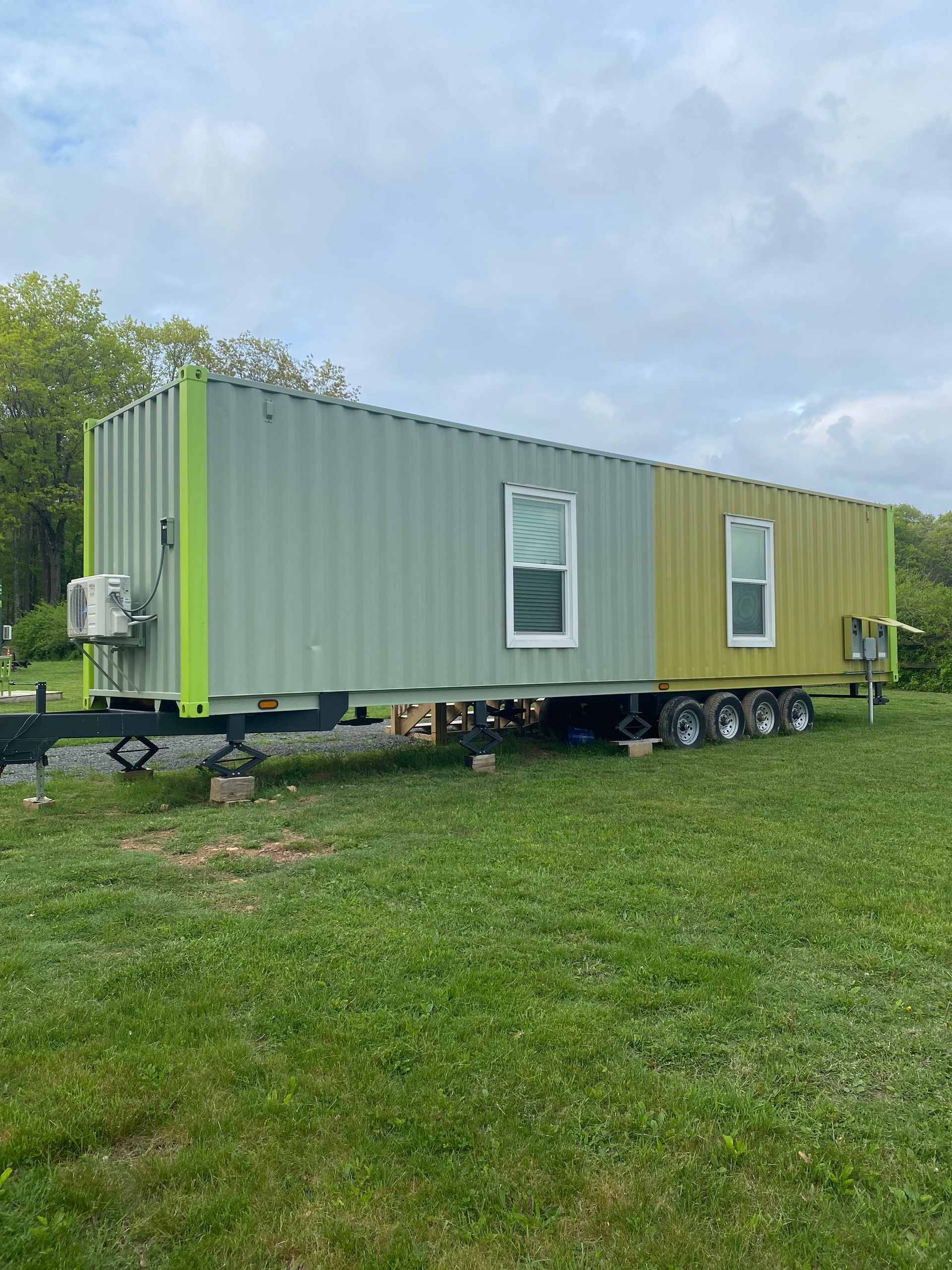 Portable patio-style food stand made from yellow and gray shipping containers on gravel, with a small porch and steps.