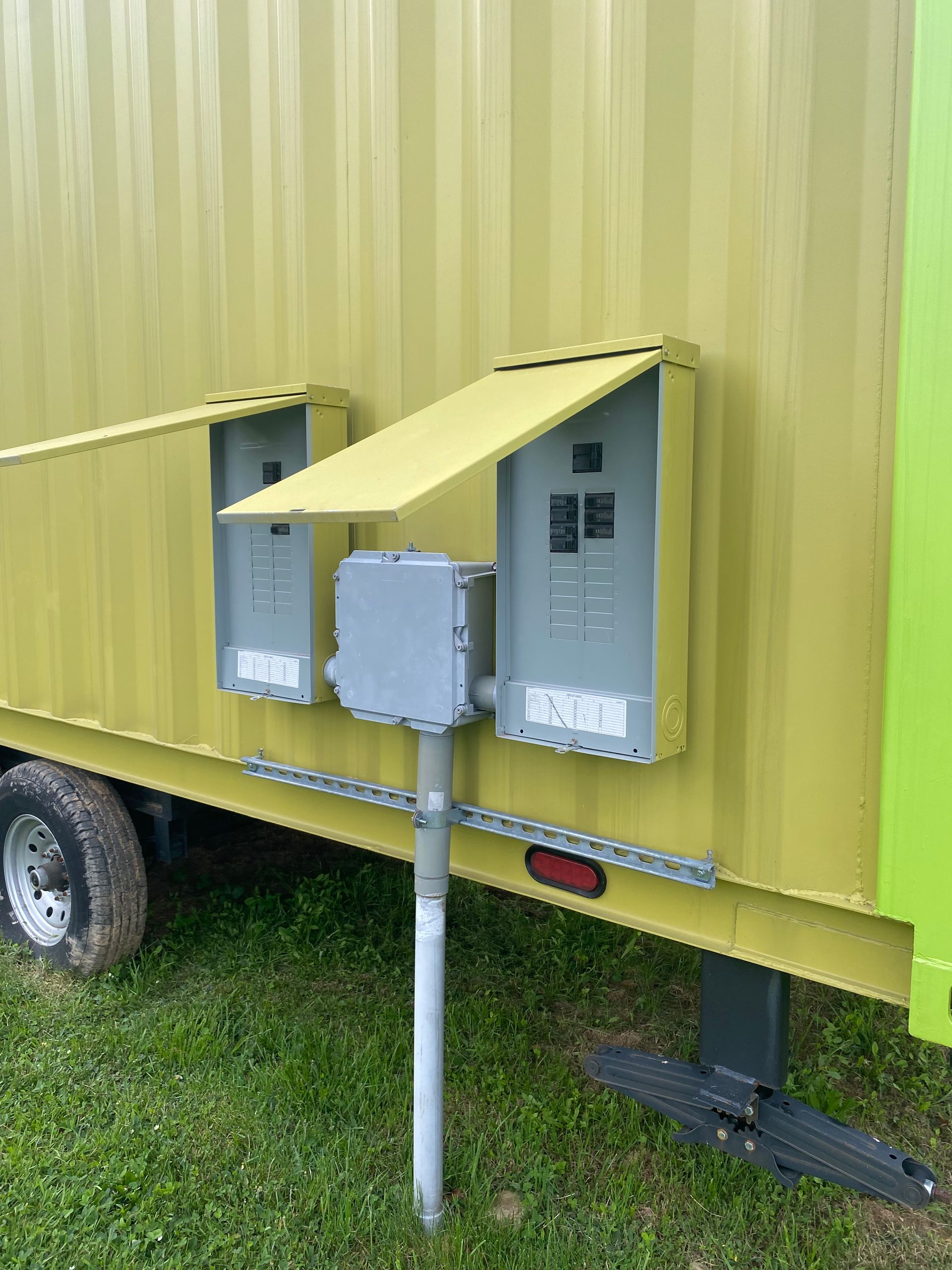 Three electrical utility boxes mounted on a yellow trailer wall with a metal support post.