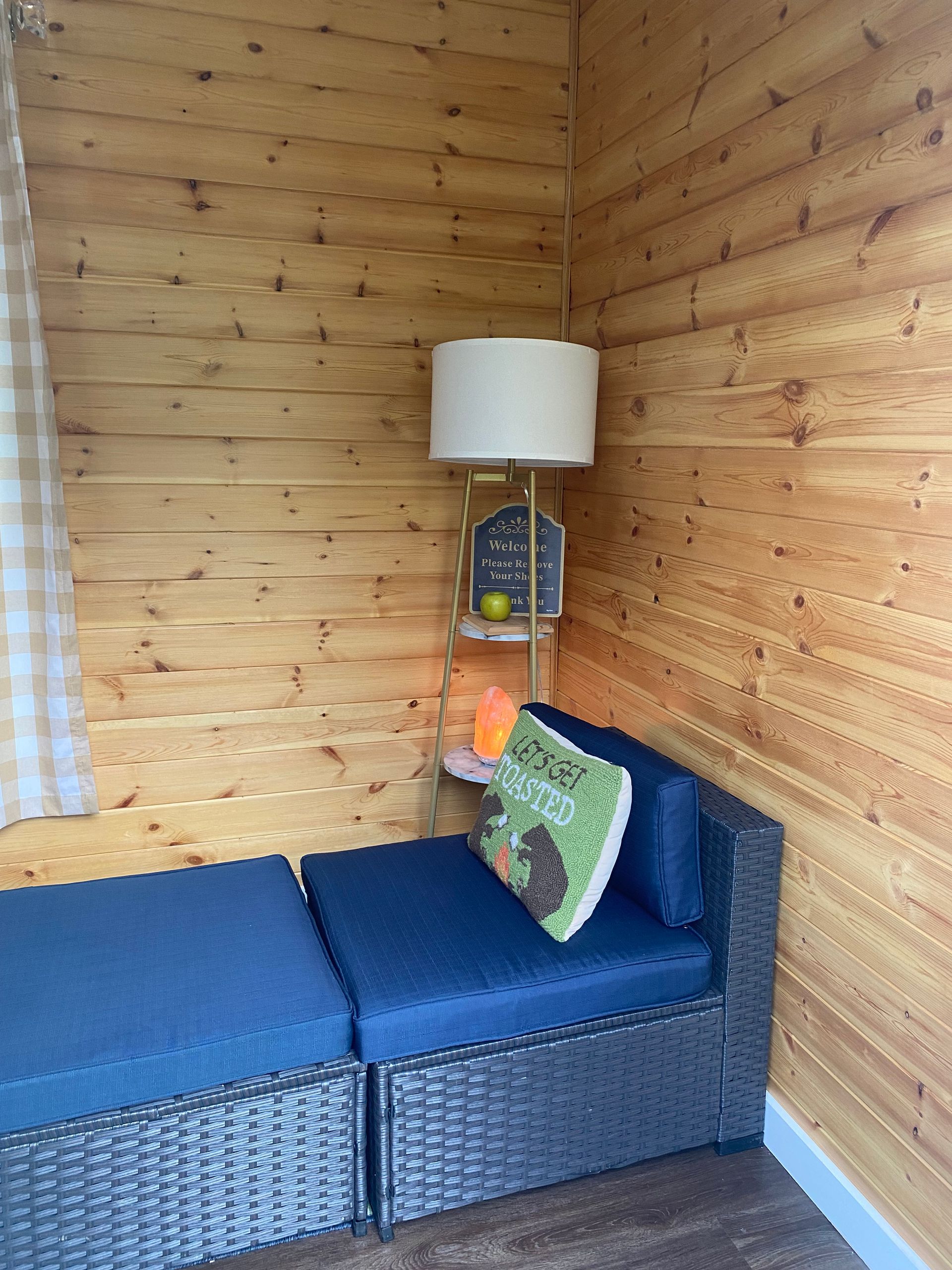 Blue wicker sofa in a wood-paneled room with a floor lamp and pillow in the corner