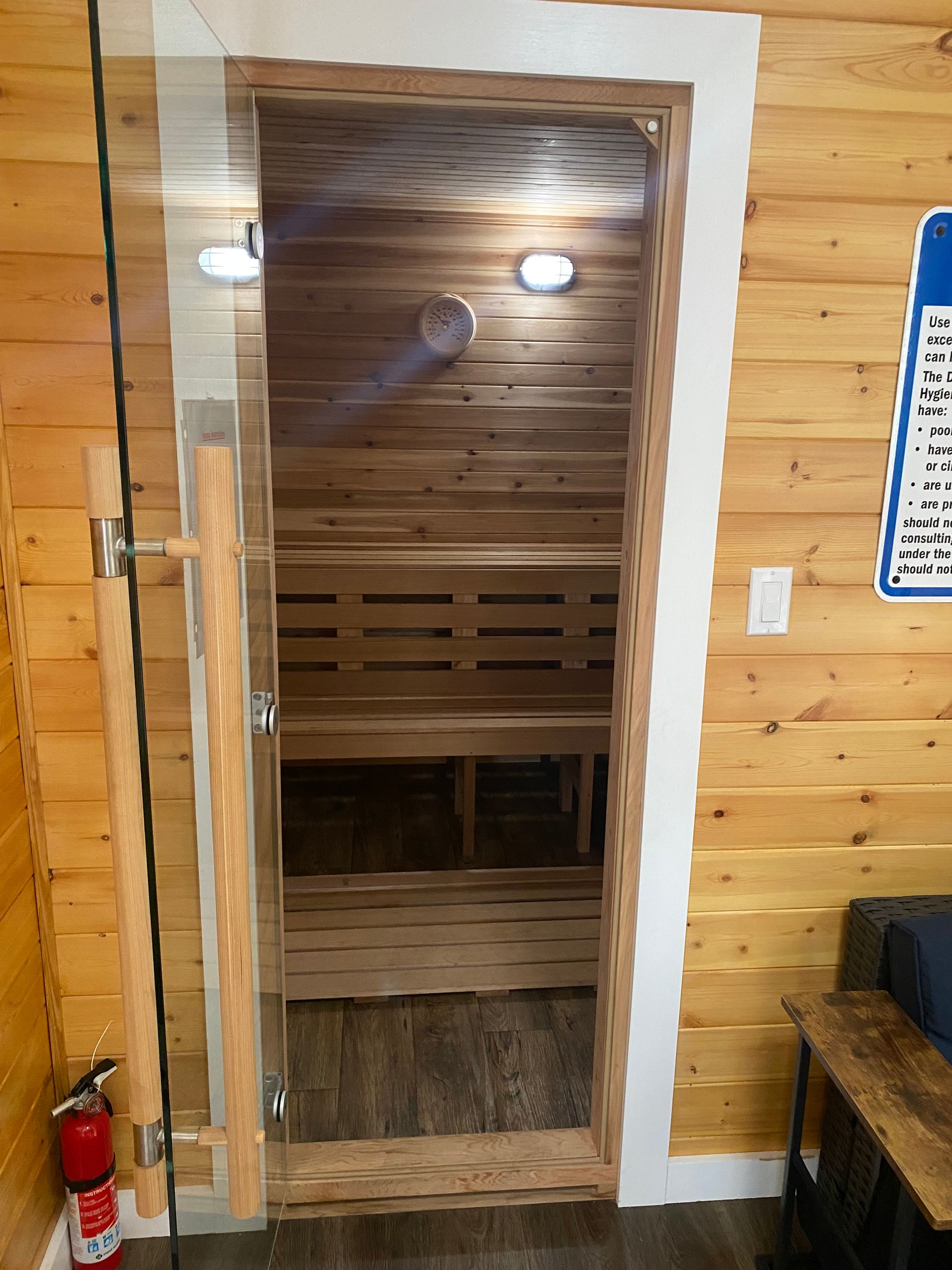 Wooden sauna doorway with white trim, lit interior, and a red fire extinguisher on the left.