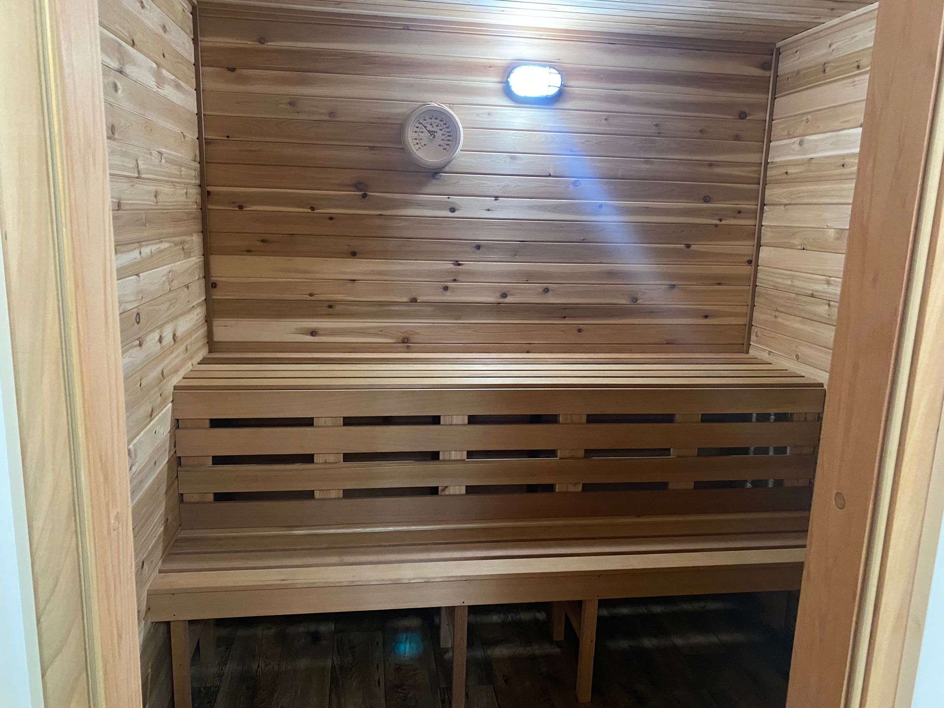 Wood-paneled sauna with a bench, wall clock, and ceiling light.