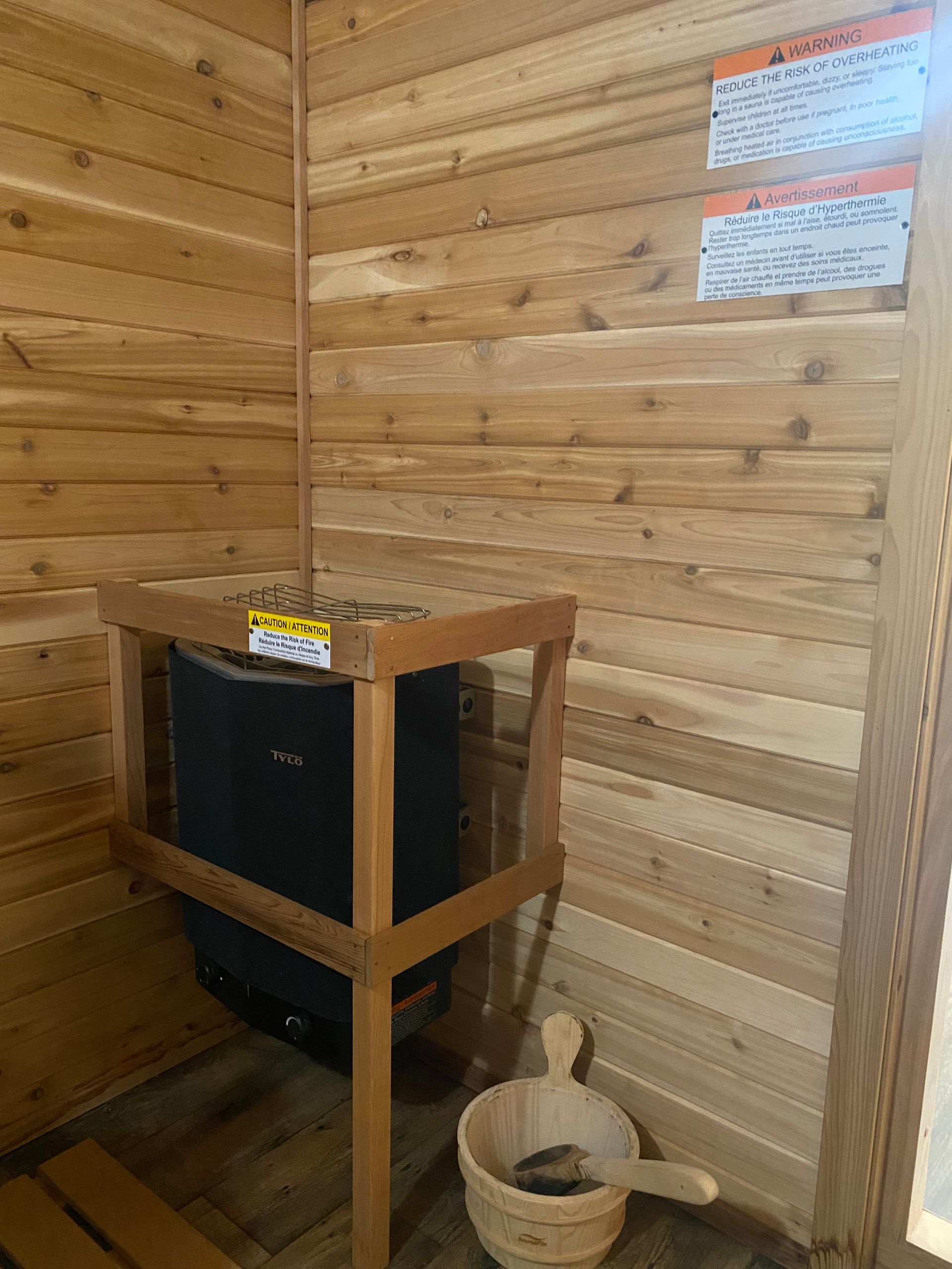Wood-paneled sauna corner with a black stove, wooden stand, and bucket and ladle on the floor
