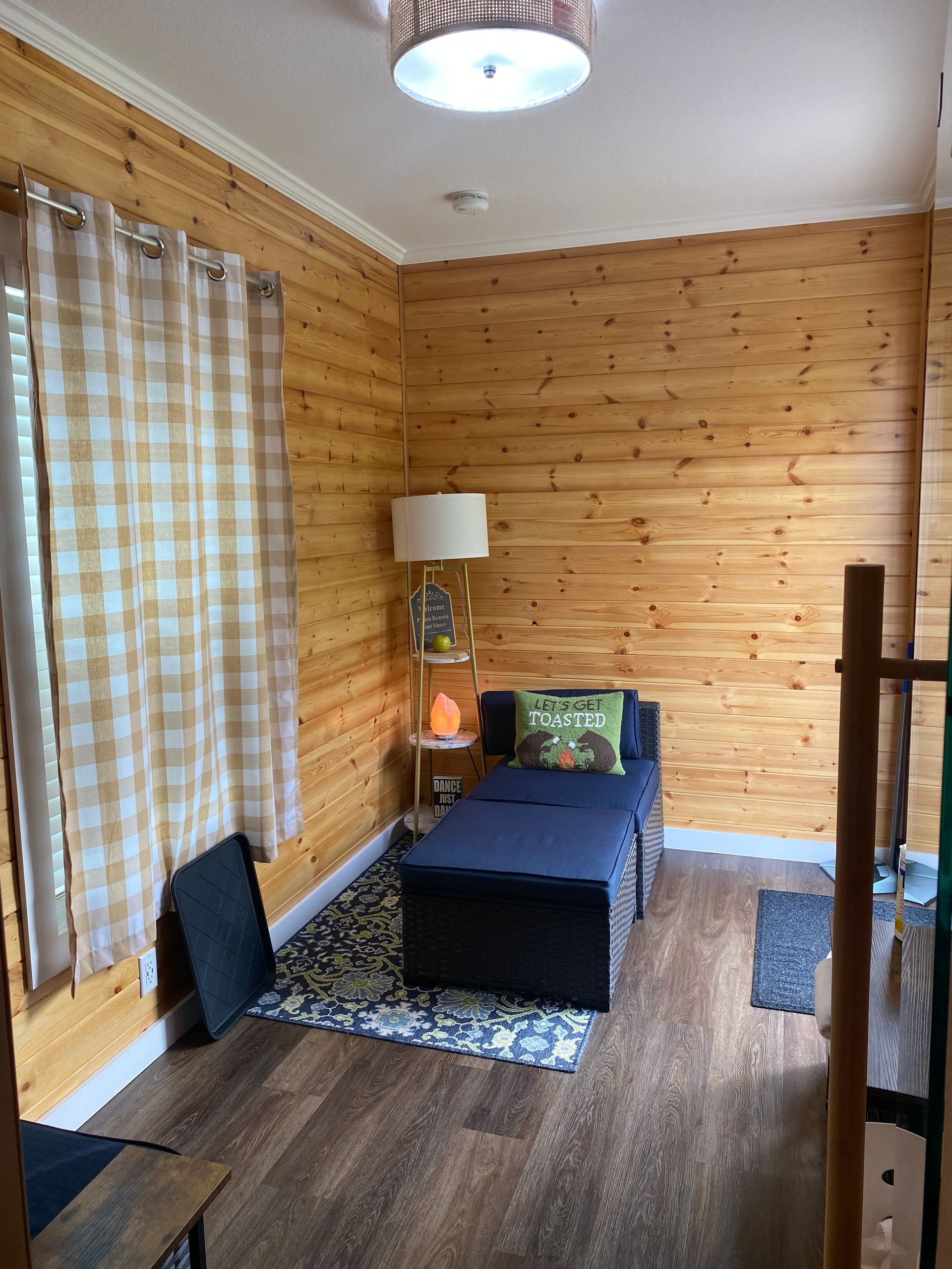 Small cozy bedroom with wood-paneled walls, single bed, lamp, and plaid curtains.