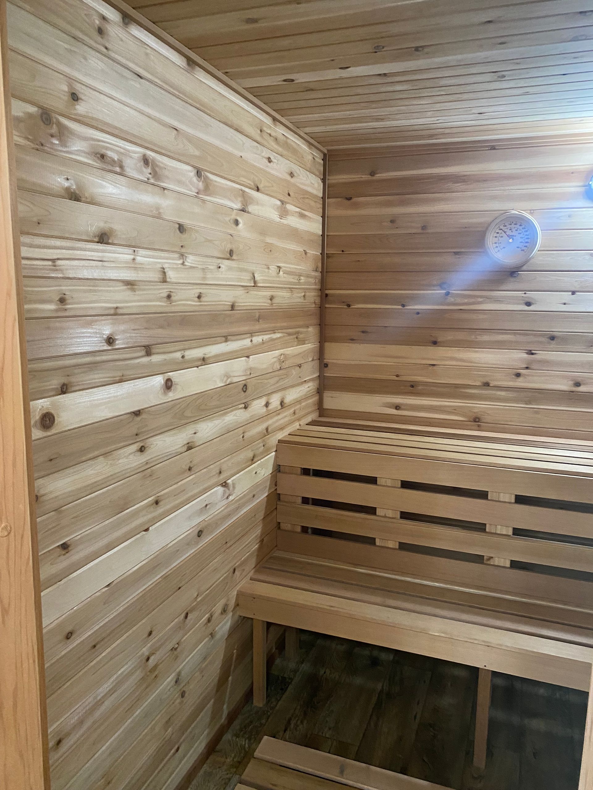 Wood-paneled sauna interior with a wooden bench and wall light, lit in warm tones