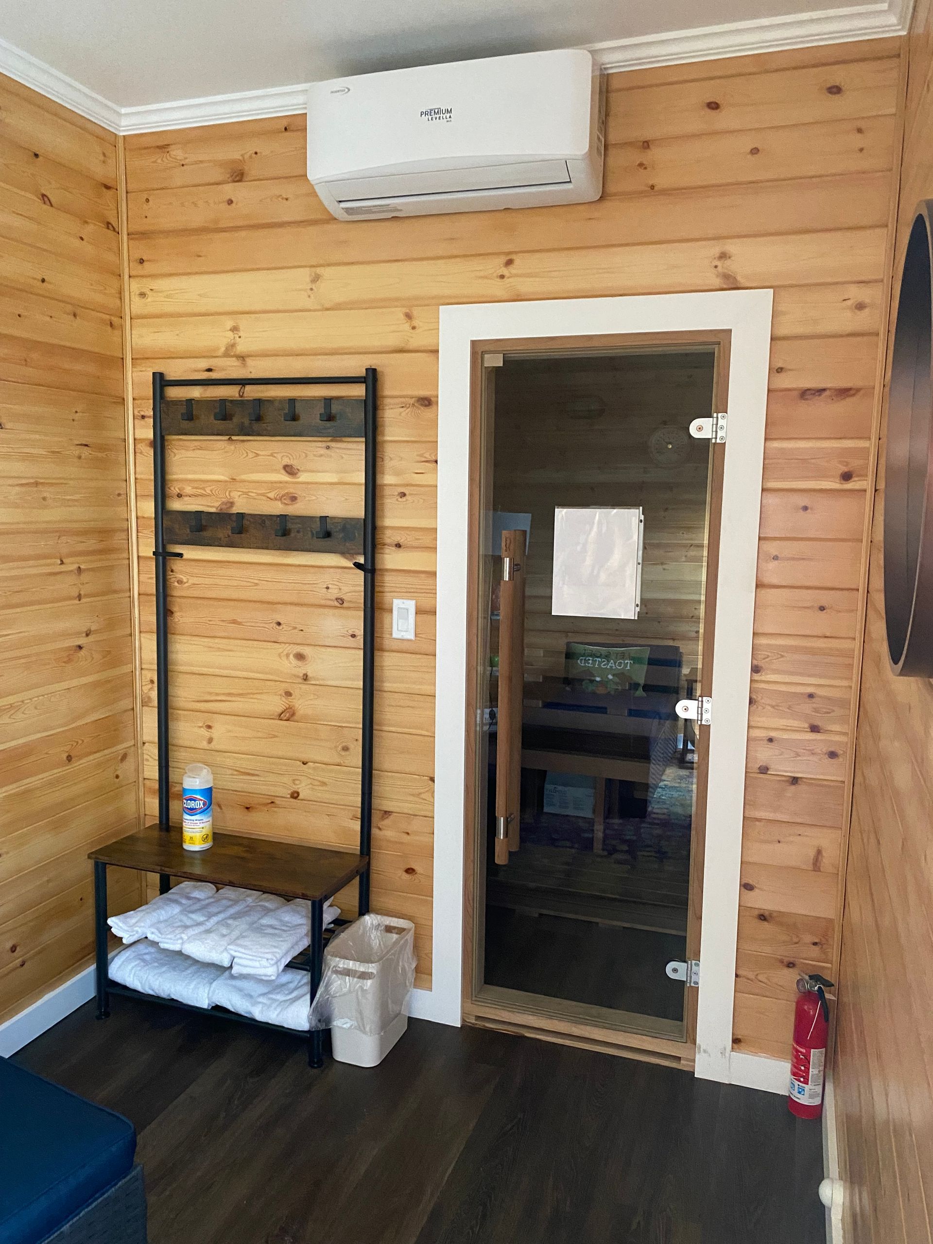 Wood-paneled room with a glass door, wall shelves, folded towels, and a small air conditioner above the doorway
