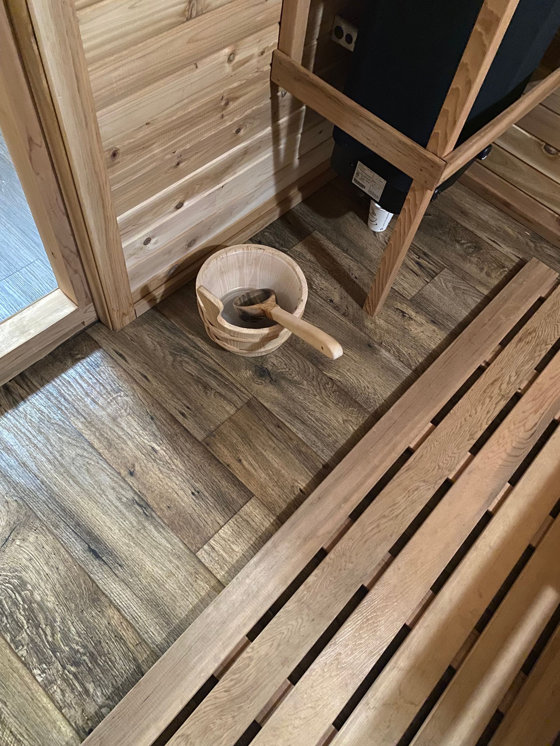 Wooden sauna bench with a bucket and ladle on the floor beside it