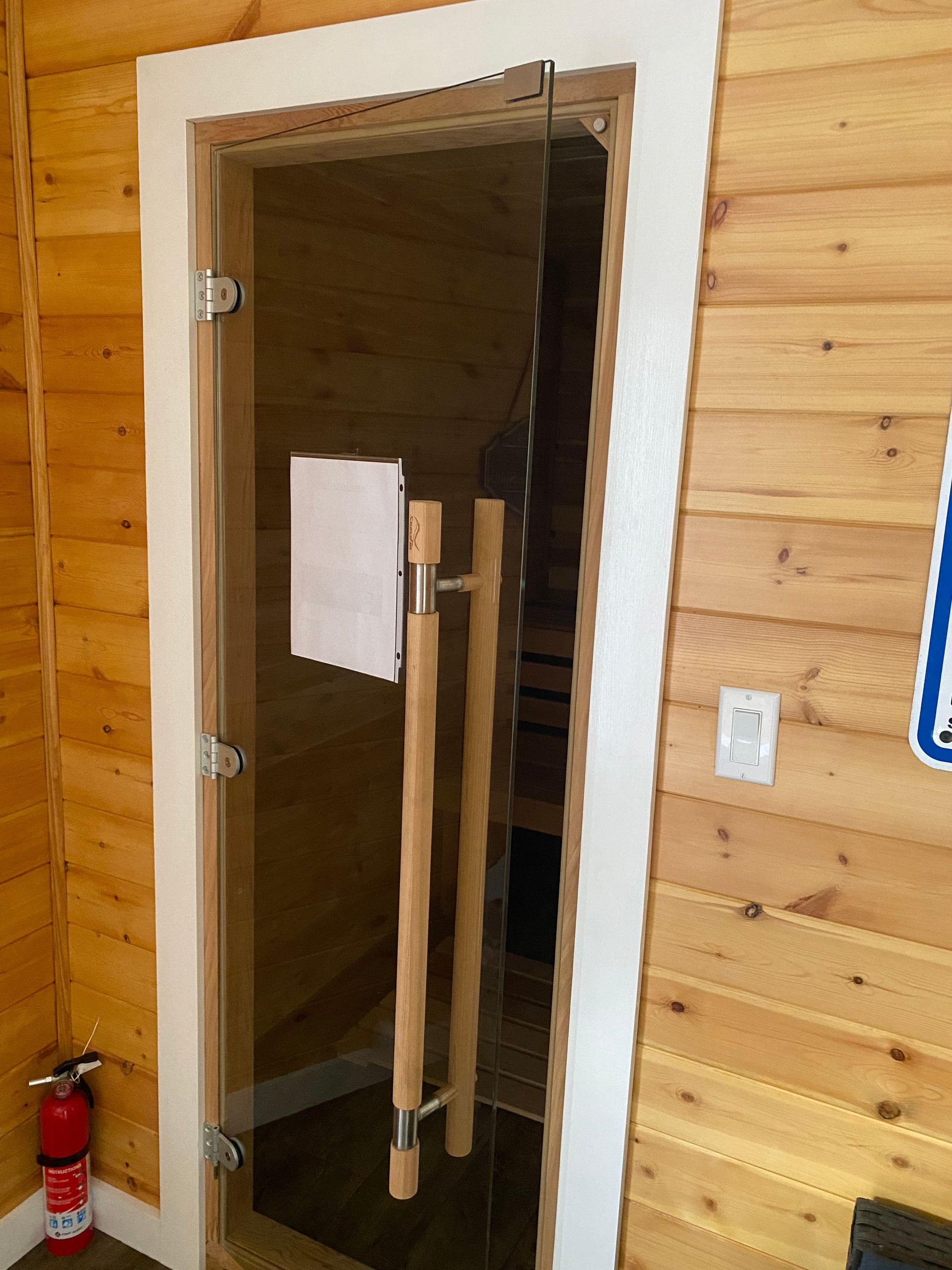 Open wooden sauna door with a towel and wooden handles inside a pine-paneled room.