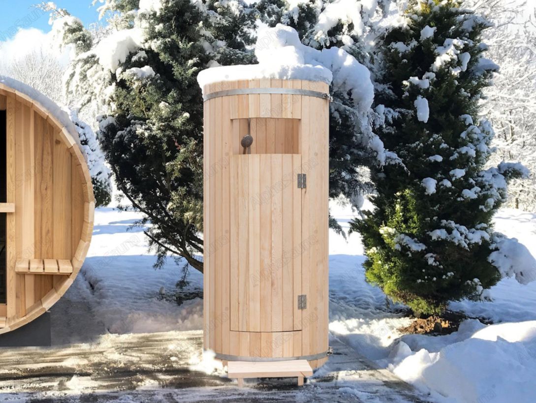 Wooden barrel sauna outdoors in snow beside evergreen trees