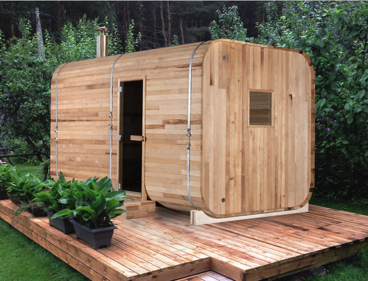 Wooden tiny house on a deck in a garden, with potted plants nearby.