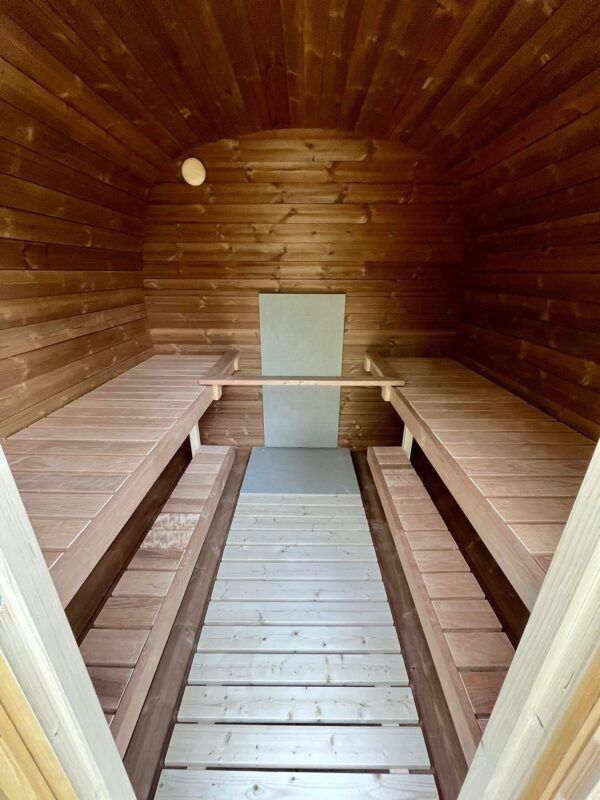 Wooden barrel sauna interior with benches on both sides and a central heater wall.