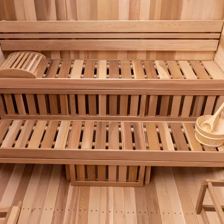 Wooden sauna interior with tiered benches, slatted walls, and a ladle and bucket on the right.