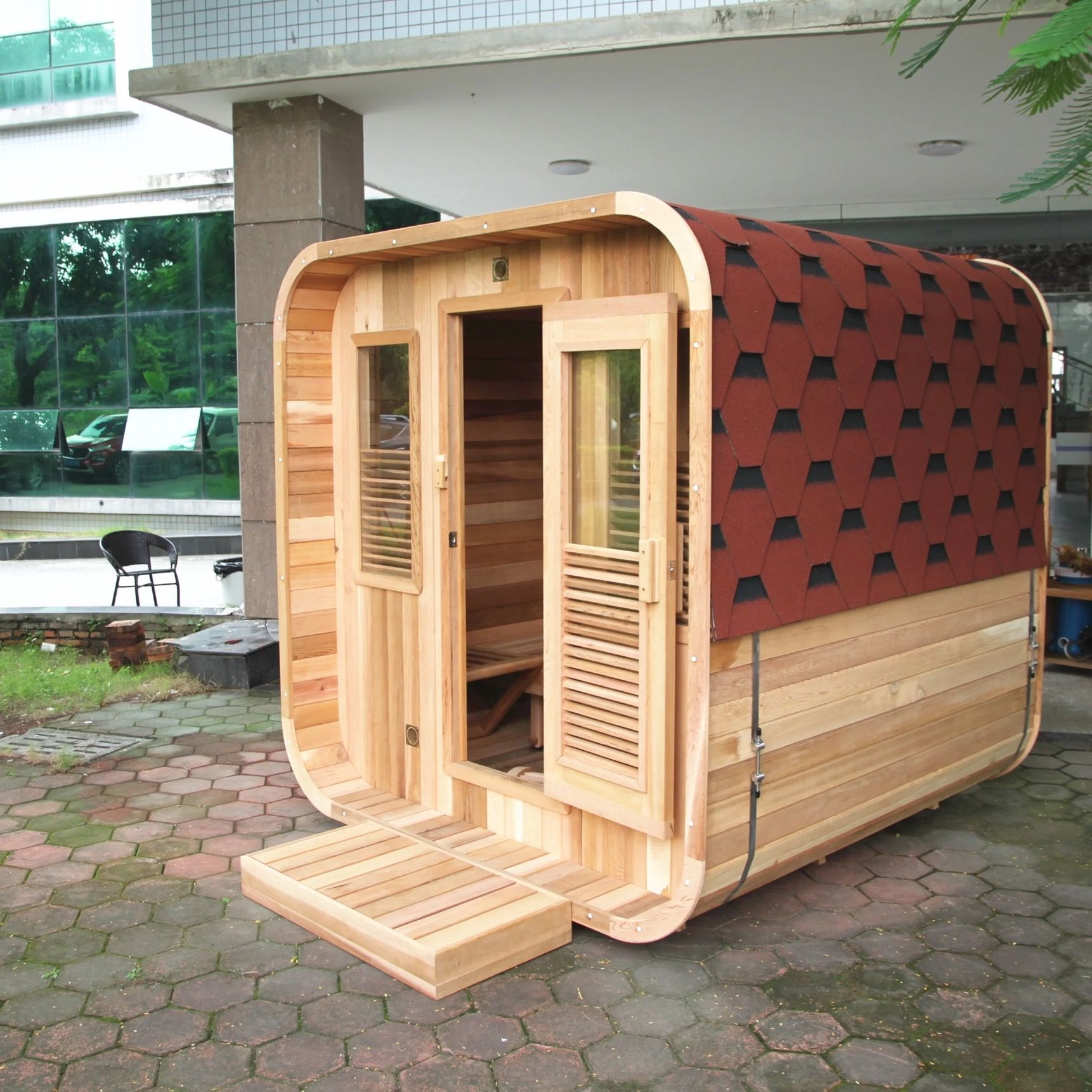 Small wooden sauna cabin with open door and step, outdoors beside a building.