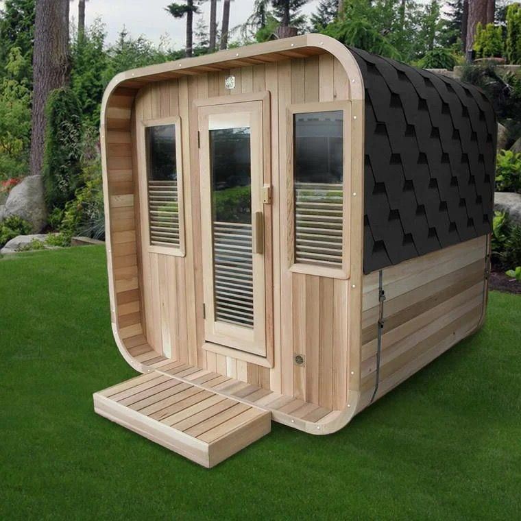 Small wooden tiny house with curved roof and black shingles, sitting on grass in a wooded yard.