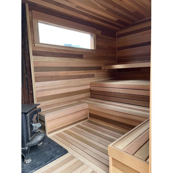 Wood-paneled sauna interior with benches, a small window, and a wood stove.