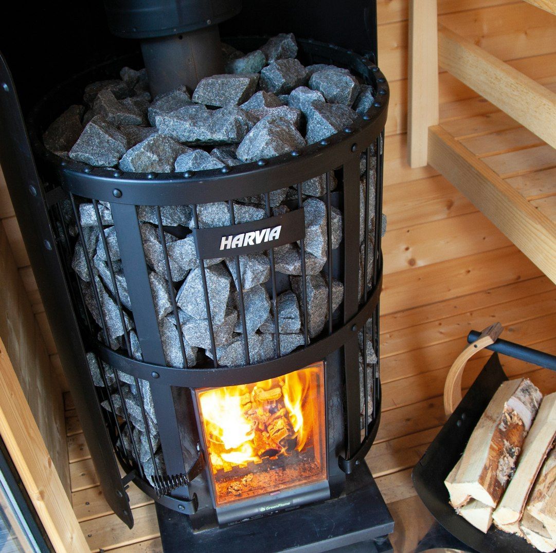 Black wood-burning stove with glowing fire and stacked stones, in a cozy wooden room