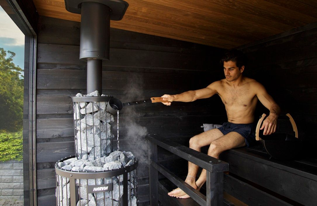 Black cylindrical sauna stove with rocks on top and a glowing firebox door.