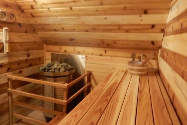 Wood-paneled sauna interior with wooden benches, rocks, and a heater in the corner
