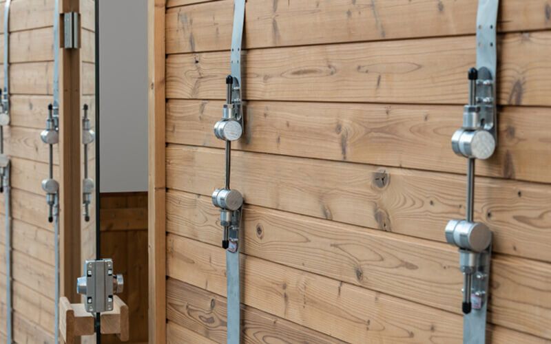 Wooden wall with several vertical metal latch mechanisms and hardware mounted in a row