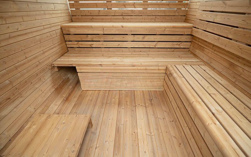 Wooden sauna interior with bench seating and warm-toned slatted walls and floor